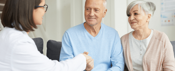 A senior couple smiling, shaking hands with a doctor at a short-term skilled nursing facility