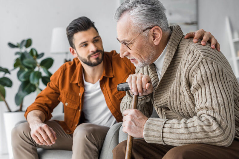 A young man attentively listens to his elderly father with a cane, embodying care for elderly parents