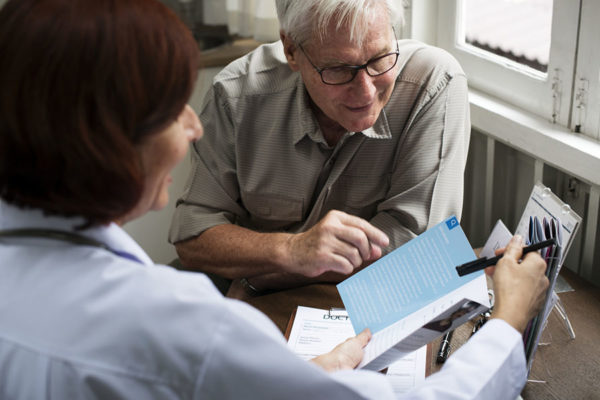 Doctor discussing speech therapy to senior man during consultation.