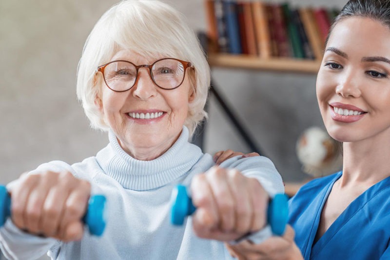 Elder female adult lifting dumbbells during her physical therapy session. Elder female adult lifting dumbbells during her physical therapy session.