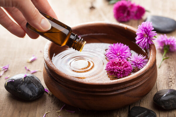 essential oil being dripped into a bowl with water and flowers for aromatherapy.