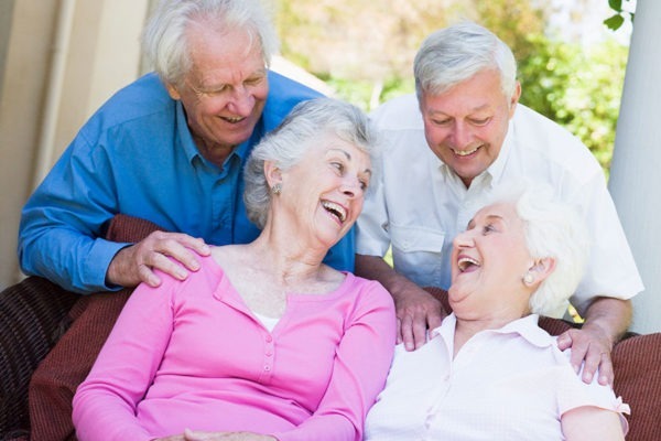 Group of senior friends sitting on the garden couch smiling at each other.