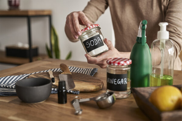 person holding a jar labeled soda among various natural cleaning supplies.