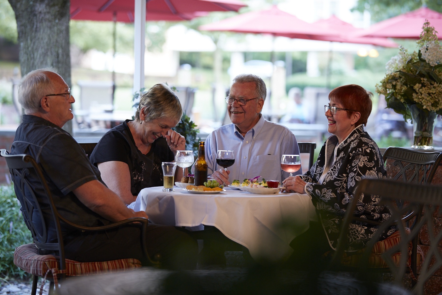 Residents from our CCRC in PA share laughter around an outdoor table with wine. Highlighting their lively community compared to traditional assisted living