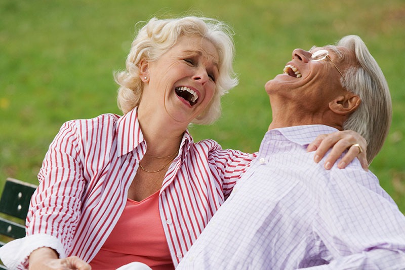 Senior couple laughing at a park bench.