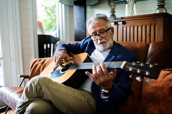 Senior man playing the guitar while sitting on the sofa.