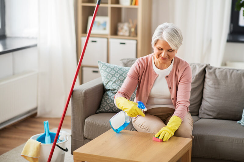 senior woman happily engaged in spring cleaning, wiping a coffee table in her living room