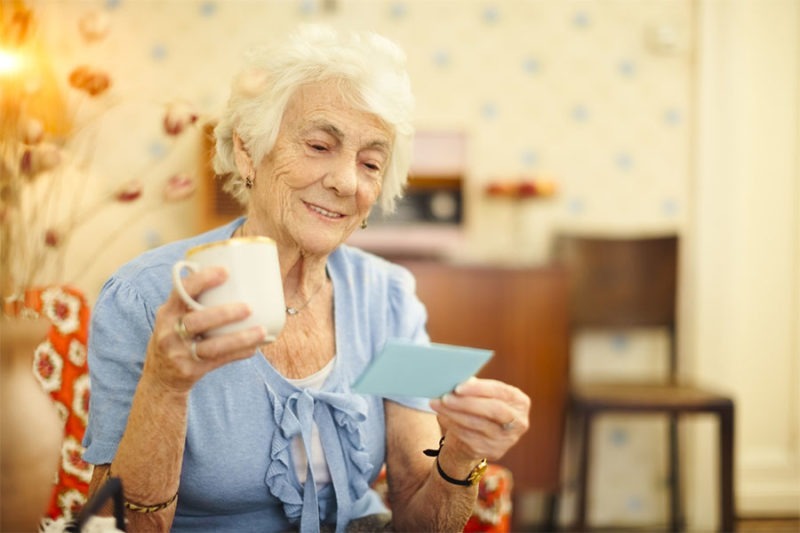 Senior woman reading the retirement card she received. Elder female adult lifting dumbbells during her physical therapy session.