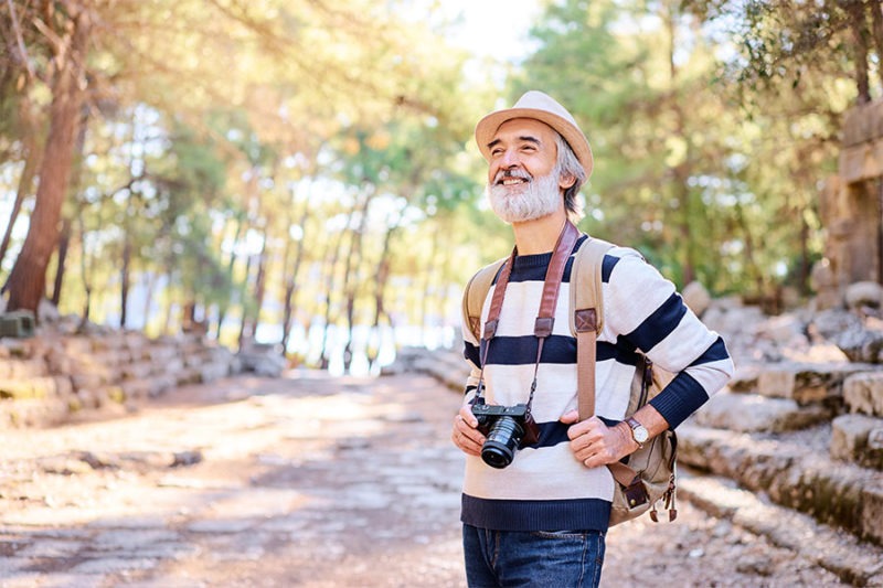 Smiling senior man holding a camera concept image for hobbies for retired men.
