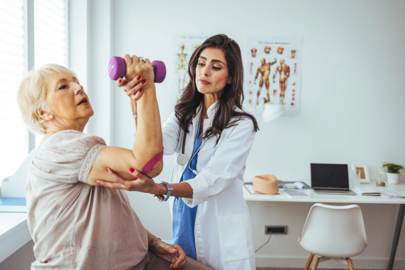 Short-Term Rehabilitation For Seniors: What To Expect 2 doctor assisting an elderly woman with arm exercises during physical therapy, an example of rehab for elderly after hospital stay