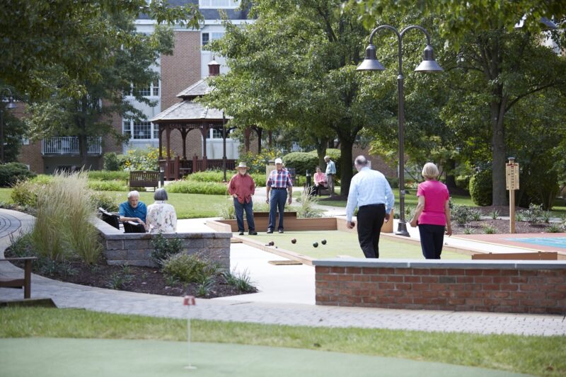 Group of residents playing bocce in the evening courtyard, highlighting summer senior living at Riddle Village