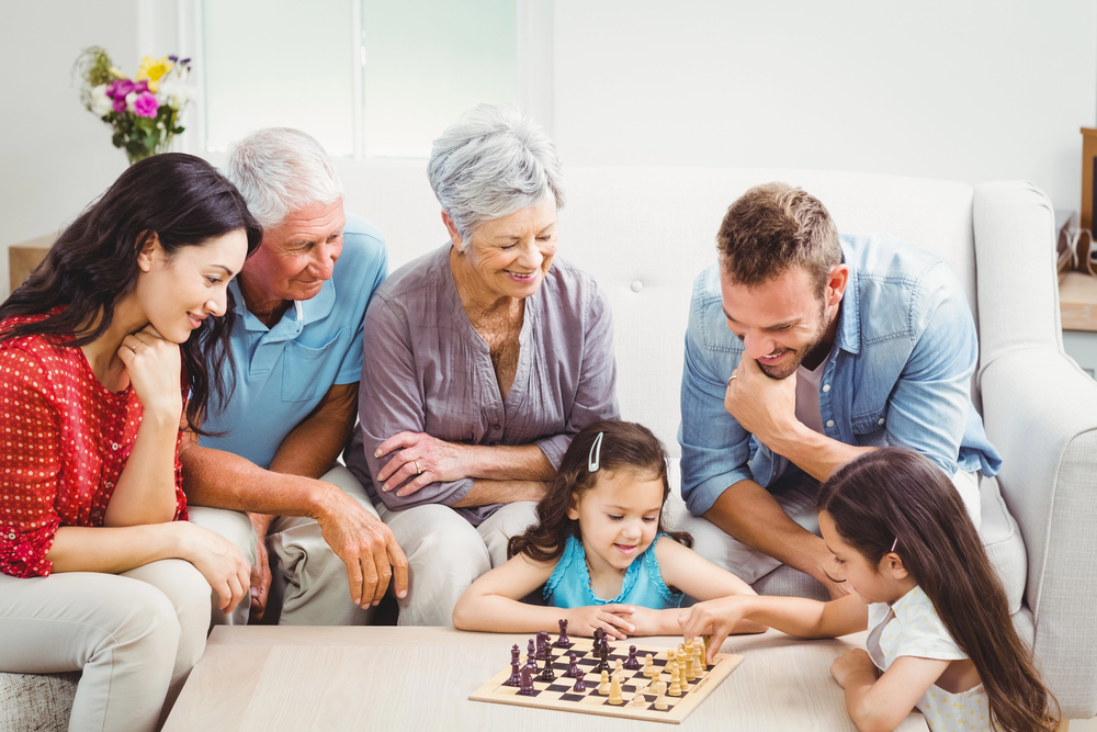 grandparents and parents smiling as they watch children play a board game